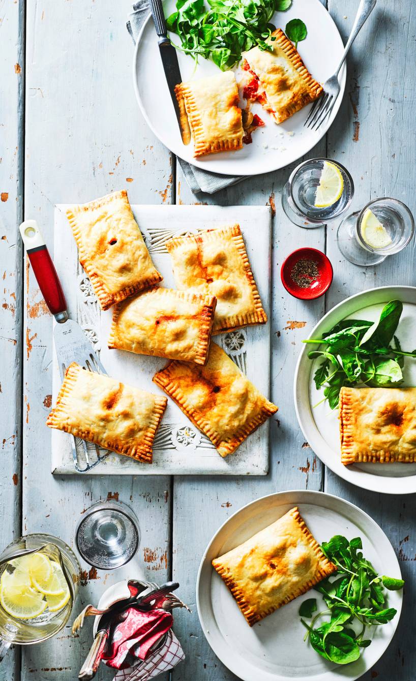 Mehrere gebackene, vegetarisch gefüllte Pizzataschen auf Tellern auf einem Tisch, daneben Salat