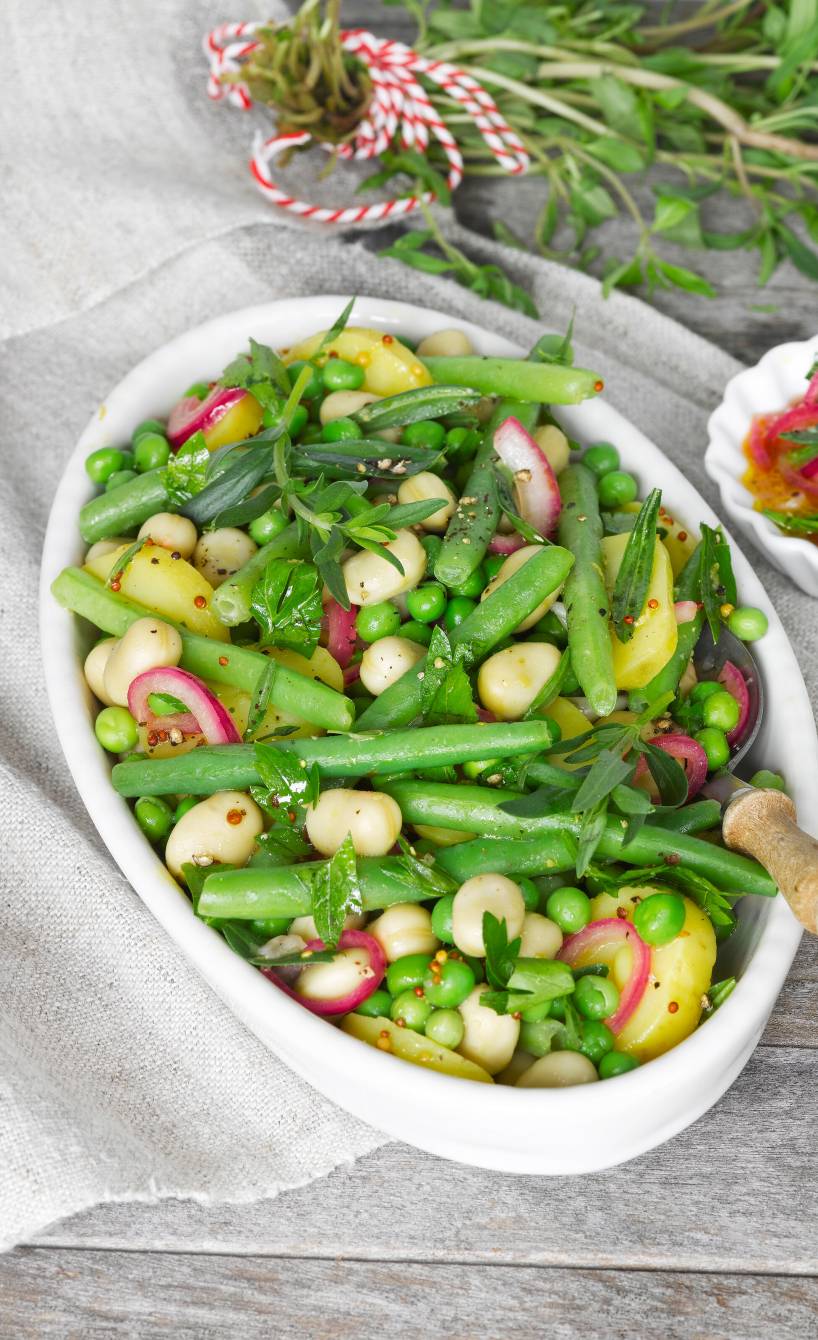 Bohnensalat aus zweierlei Bohnen mit Kartoffeln und Erbsen angerichtet auf einer Servierplatte, daneben Vinaigrette
