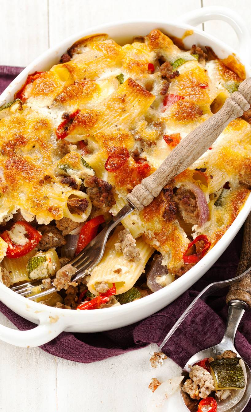 Eine Auflaufform mit Nudelauflauf mit Hackfleisch und Gemüse steht auf einem weißen Holztisch