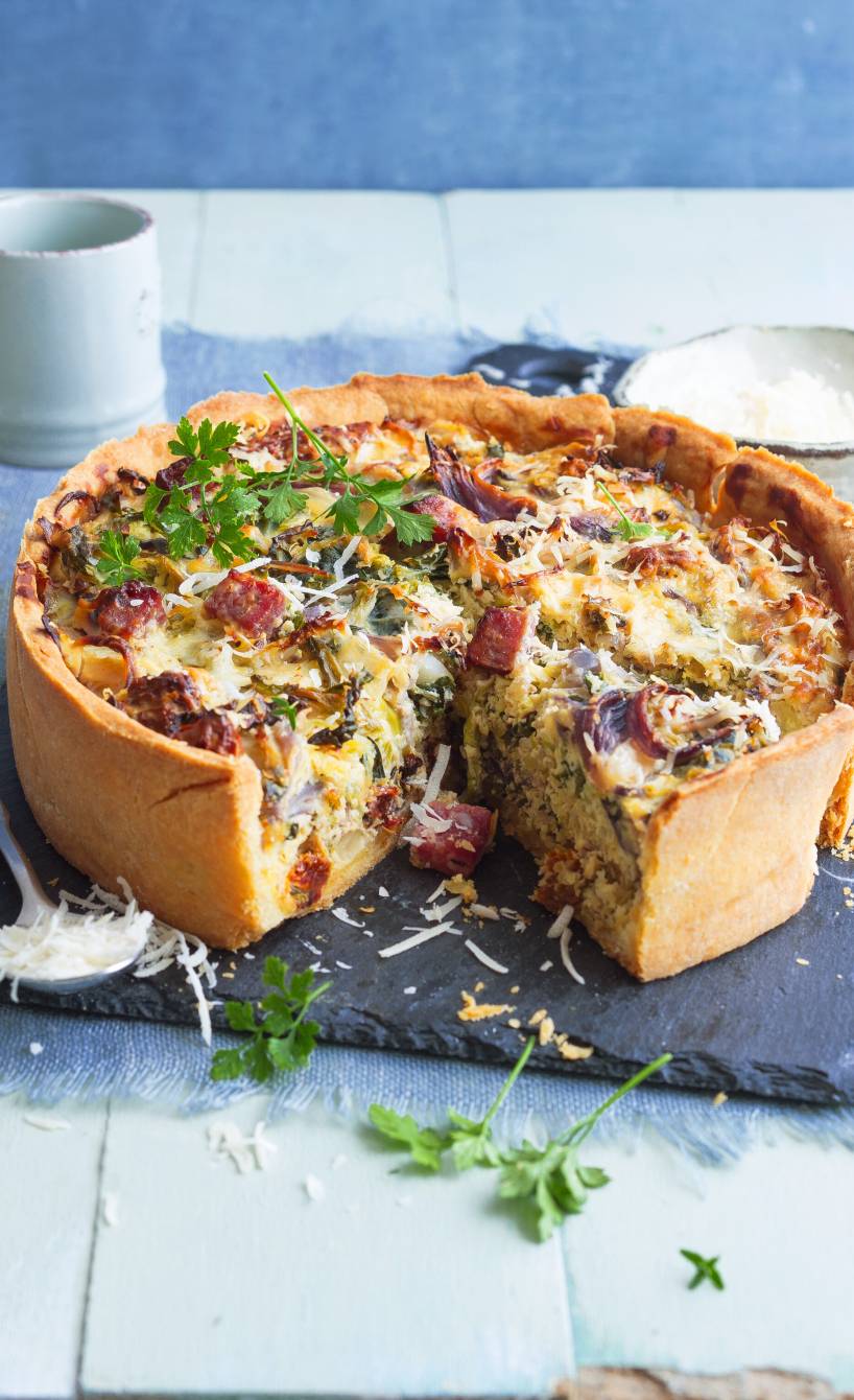 Wirsingkuchen mit Salami und Ricotta angeschnitten auf einem Schieferbrett getoppt von Parmesan