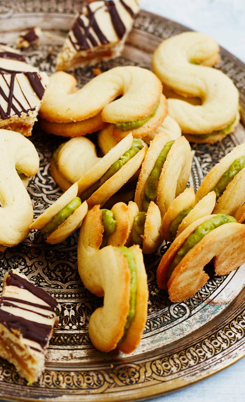 Doppeldecker-Spritzgebäck gefüllt mit Pistaziencreme auf einem Plätzchenteller neben anderen Weihachtsplätzchen