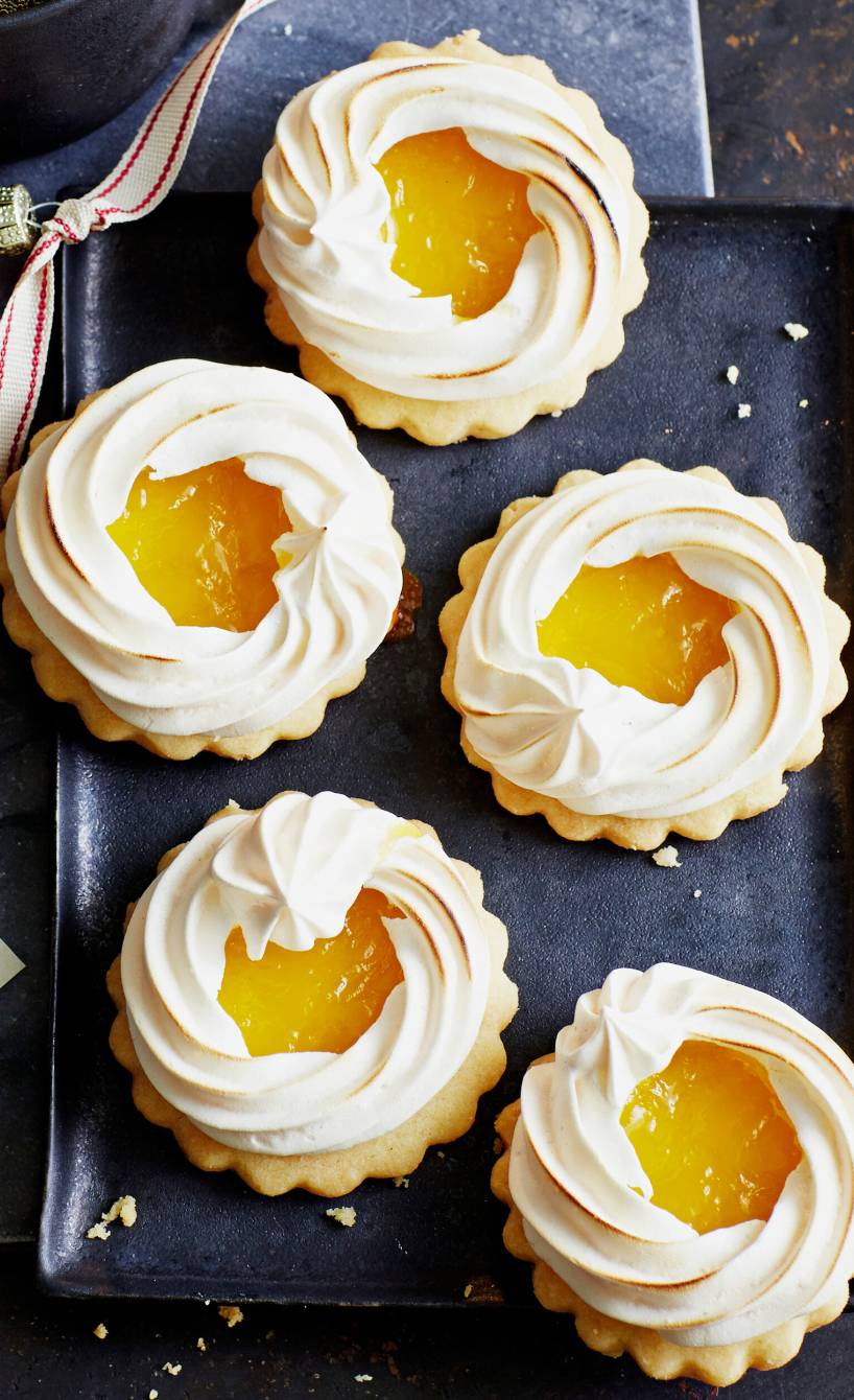 Runde Zitronenplätzchen mit Baiser auf einer schwarzen Kuchenplatte