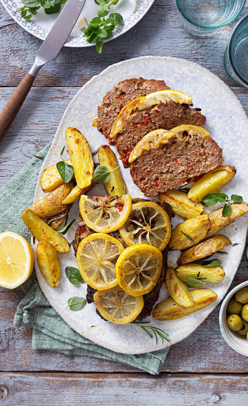 Hackbraten angeschnitten auf einer Servierplatte mit Rosmarinkartoffeln und gebackenen Zitronenscheiben