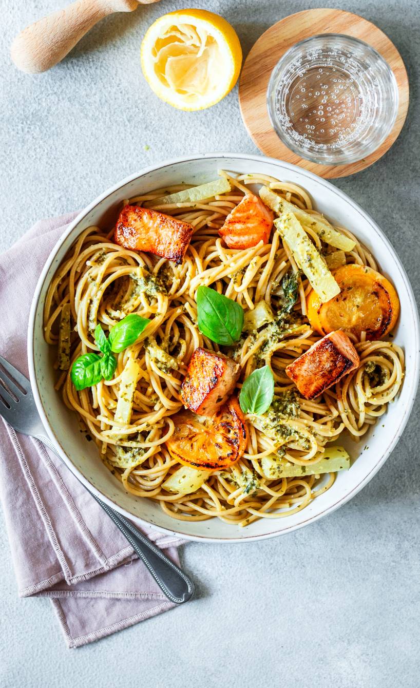 Vollkornspaghetti mit gebratenen Lachsfiletstücken und Zitronen-Sahnesoße getoppt von frischem Basilikum auf einem Pastateller