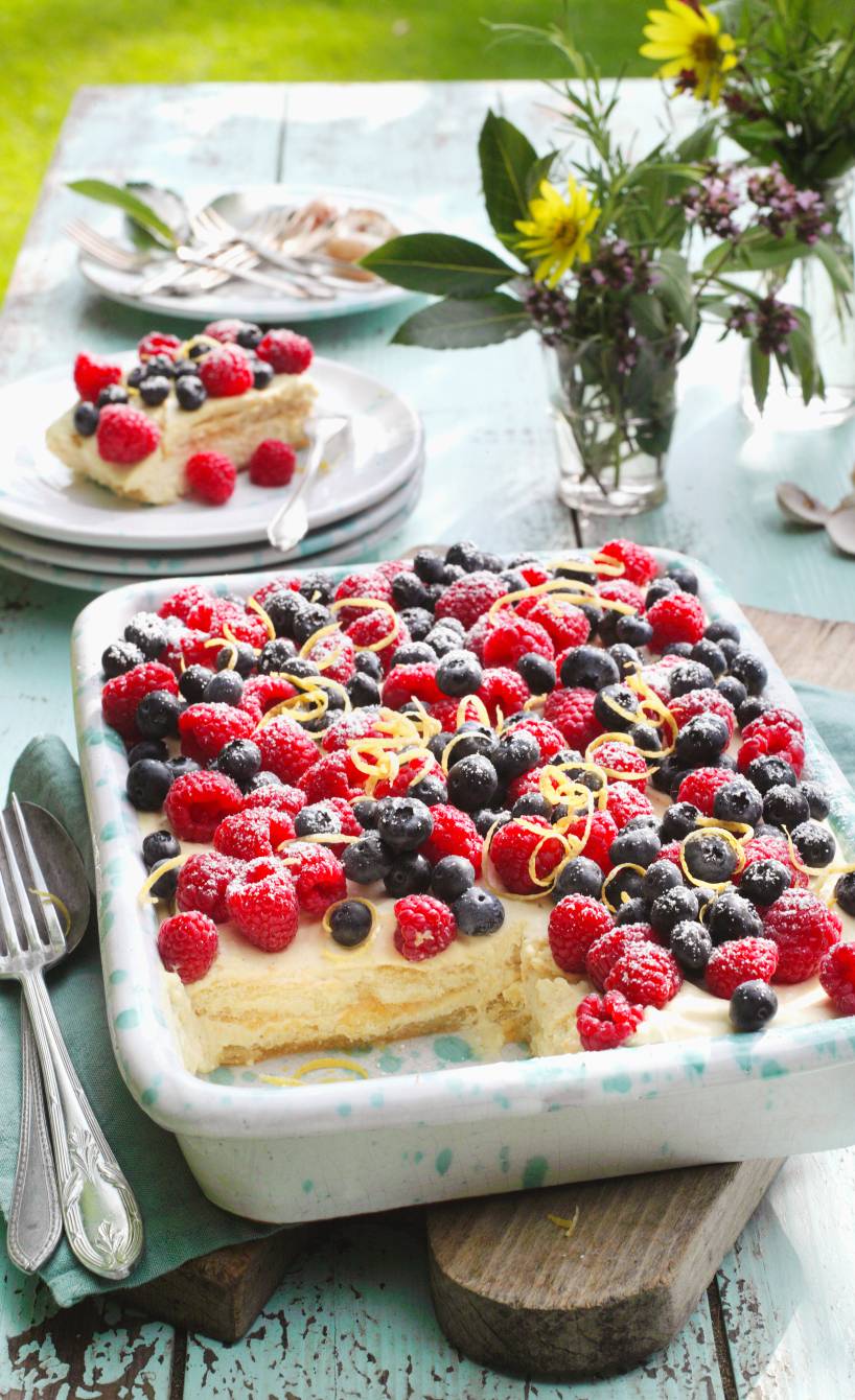 Zitronentiramisu angeschnitten in einer Auflaufform garniert mit verschiedenen Beeren auf einem Tisch im Grünen
