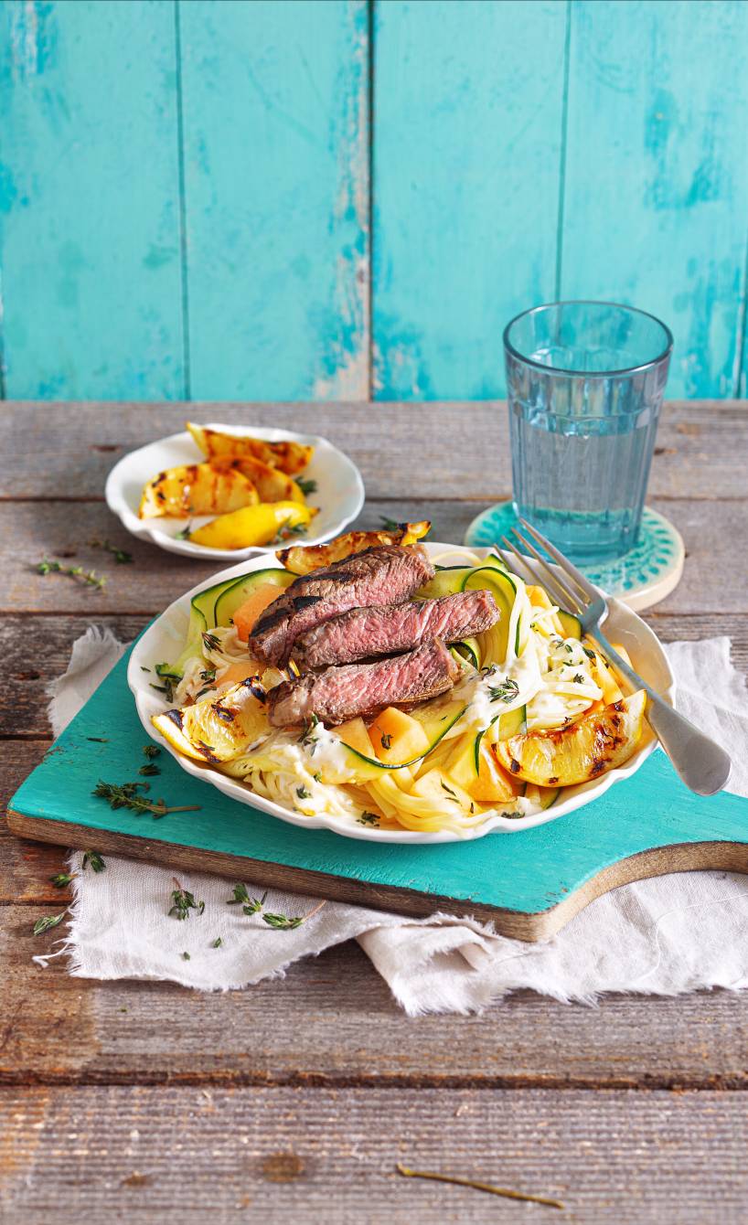 Linguine und Zucchini auf einem Teller, darauf gegrilltes Steak und Melonenstücke