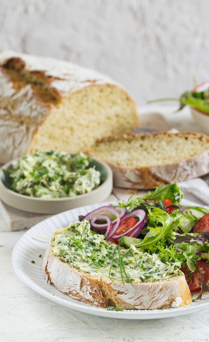 Zucchinibrot angeschnitten auf einem Tisch, einige Scheiben serviert auf einem Teller mit Salat und Aufstrich