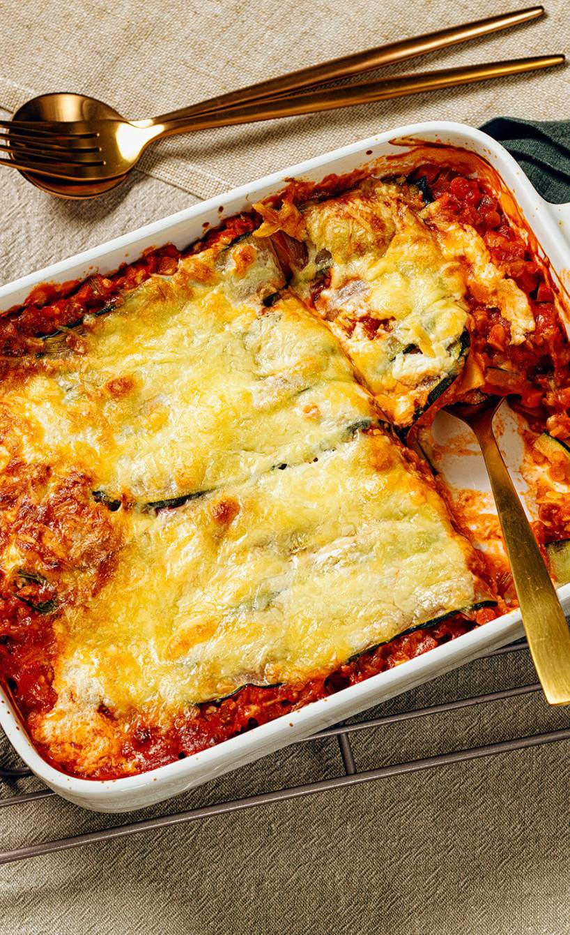 Vegetarische Zucchinilasagne in einer Auflaufform, ein Stück auf einem Teller daneben