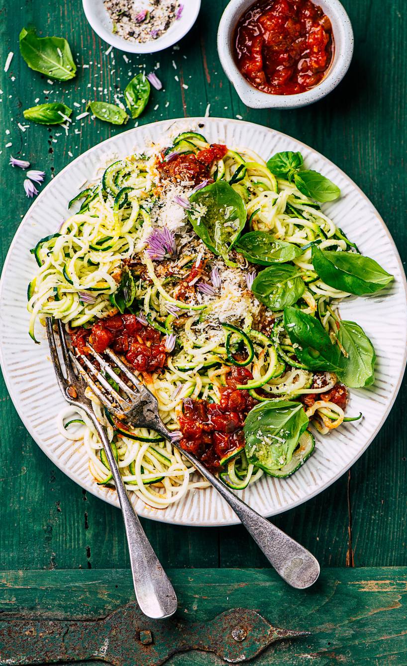 Low-Carb-Zucchinispaghetti angerichtet mit Tomatensoße und Basilikumpesto auf einem Pastateller