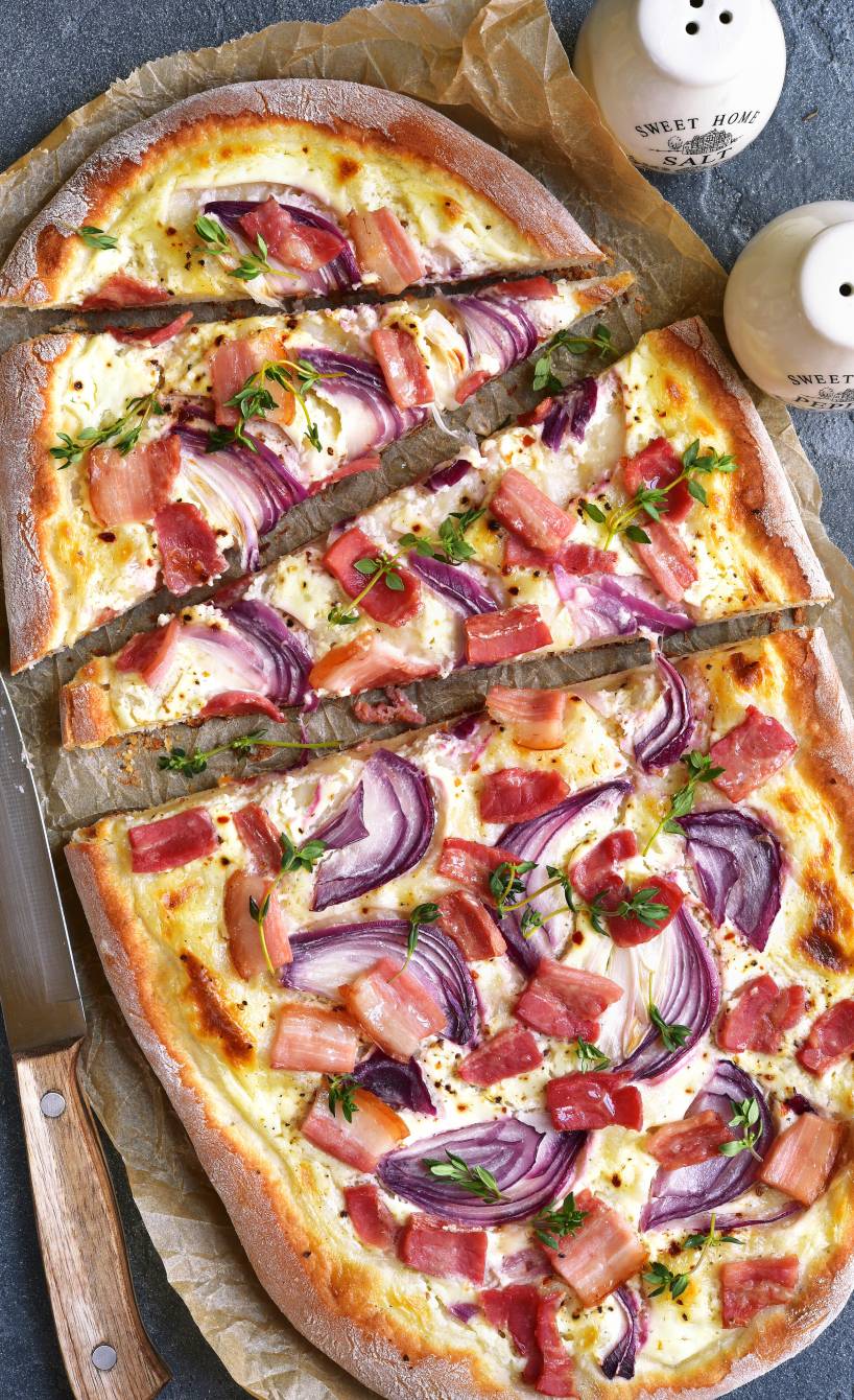 Zwiebelpizza mit Pancetta, Mascarpone und Mozzarella angeschnitten auf einem Stück Backpapier