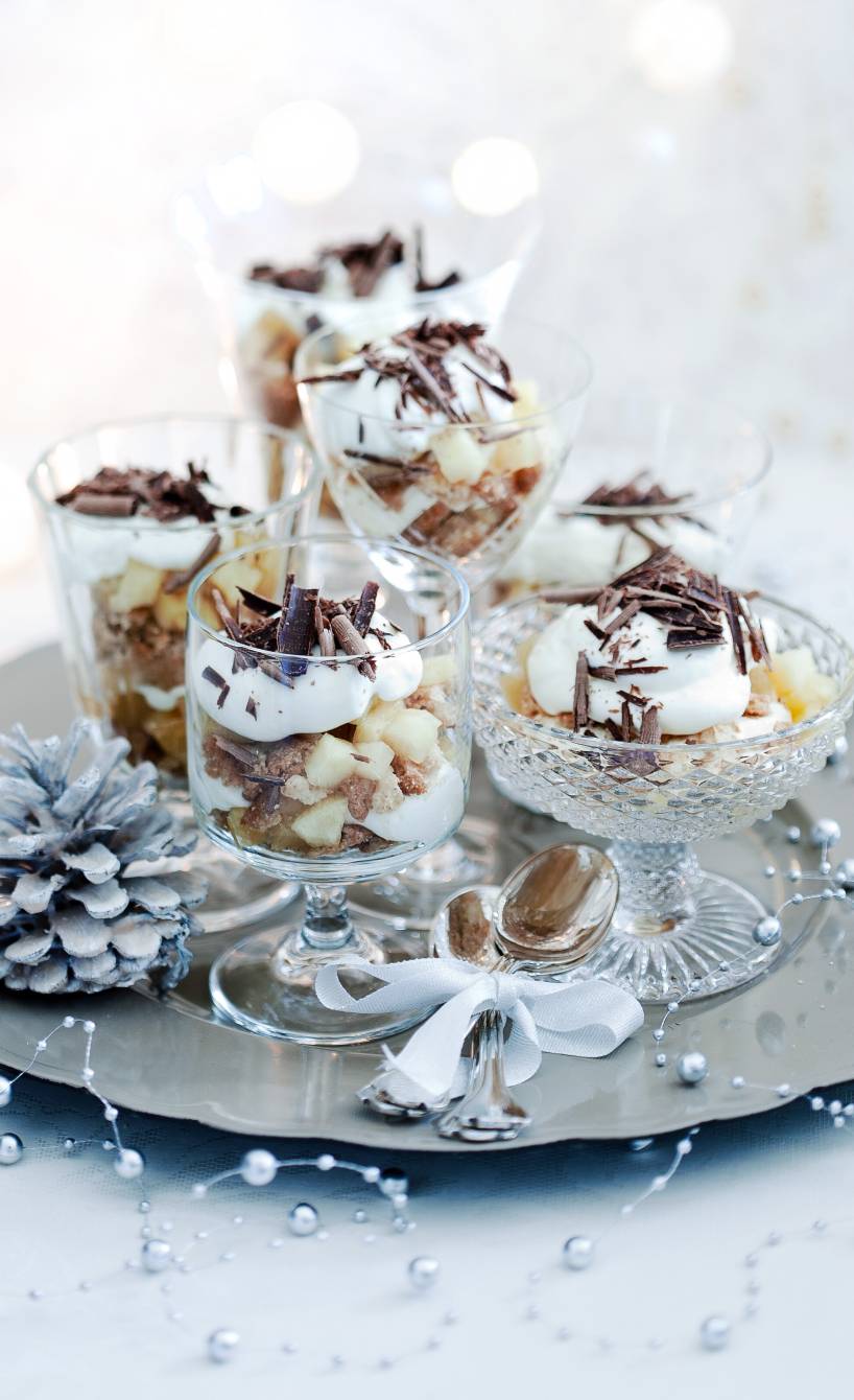 Mehrere Apfel-Mascarpone-Schichtdesserts in unterschiedlichen Gläsern auf einer silbernen Platte auf einem weihnachtlich dekorieren Tisch