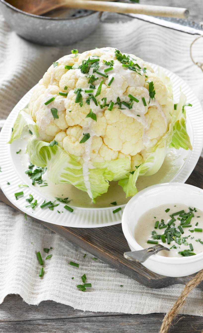 Ganzer, dampfgegarter Blumenkohl auf einem Teller übergossen mit italienischer Mandel-Knoblauch-Soße