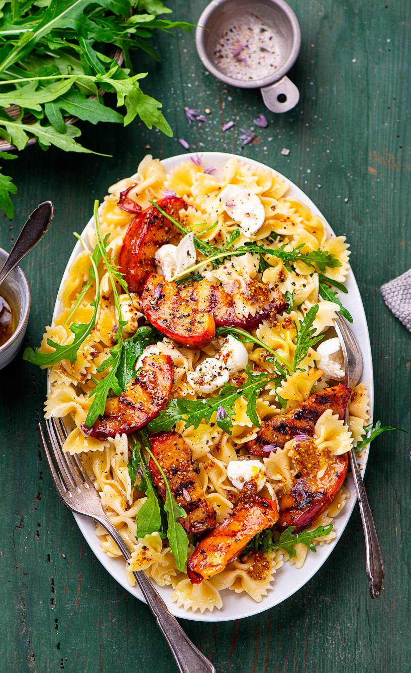 Nudelsalat mit gegrillten Nektarinen, Rucola und Mozzarella angerichtet auf einer Servierplatte