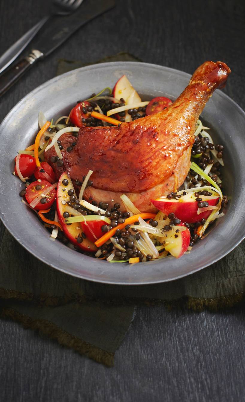 Eine Entenkeule angerichtet auf Linsen-Apfel-Gemüse mit Tomaten auf einem Teller