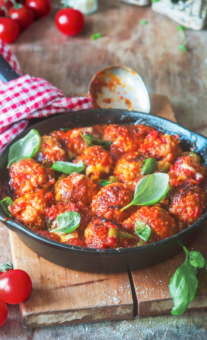 Hackfleischbällchen in Tomatensugo in einer Pfanne auf einem Tisch umringt von frischen Zutaten