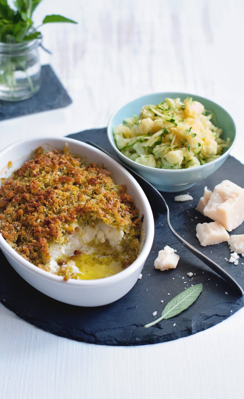 Kabeljau mit Kräuter-Parmesan-Kruste in einer Auflaufform, daneben eine Schale mit Zucchini-Stampfkartoffeln und Parmesan