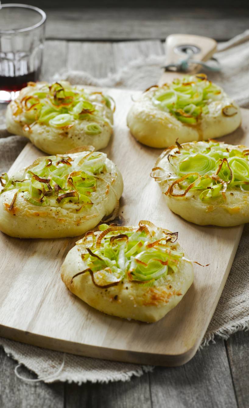 Fünf Mini-Pizzen belegt mit Lauch und Mascarpone auf einem Holzbrett