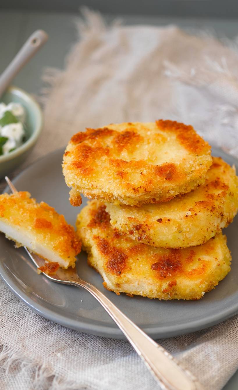Drei panierte, goldbraune Sellerieschnitzel gestapelt auf einem Teller, daneben ein Dip