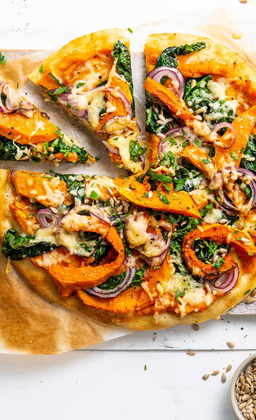 Pizza belegt mit Kürbisspalten, Spinat und Käse angeschnitten auf einem Teller