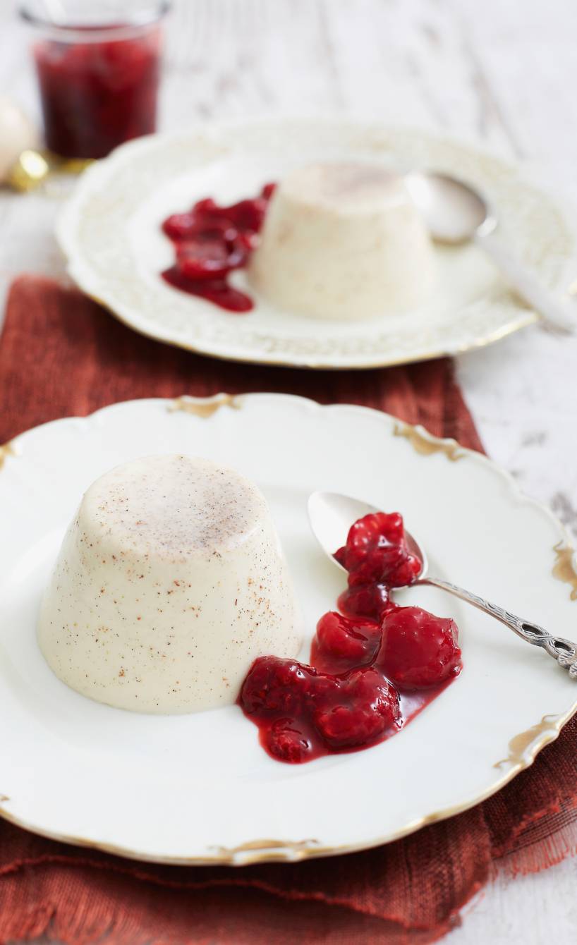 Zwei Törtchen Lebkuchen Panna cotta auf Desserttellern, daneben heißen Himbeeren