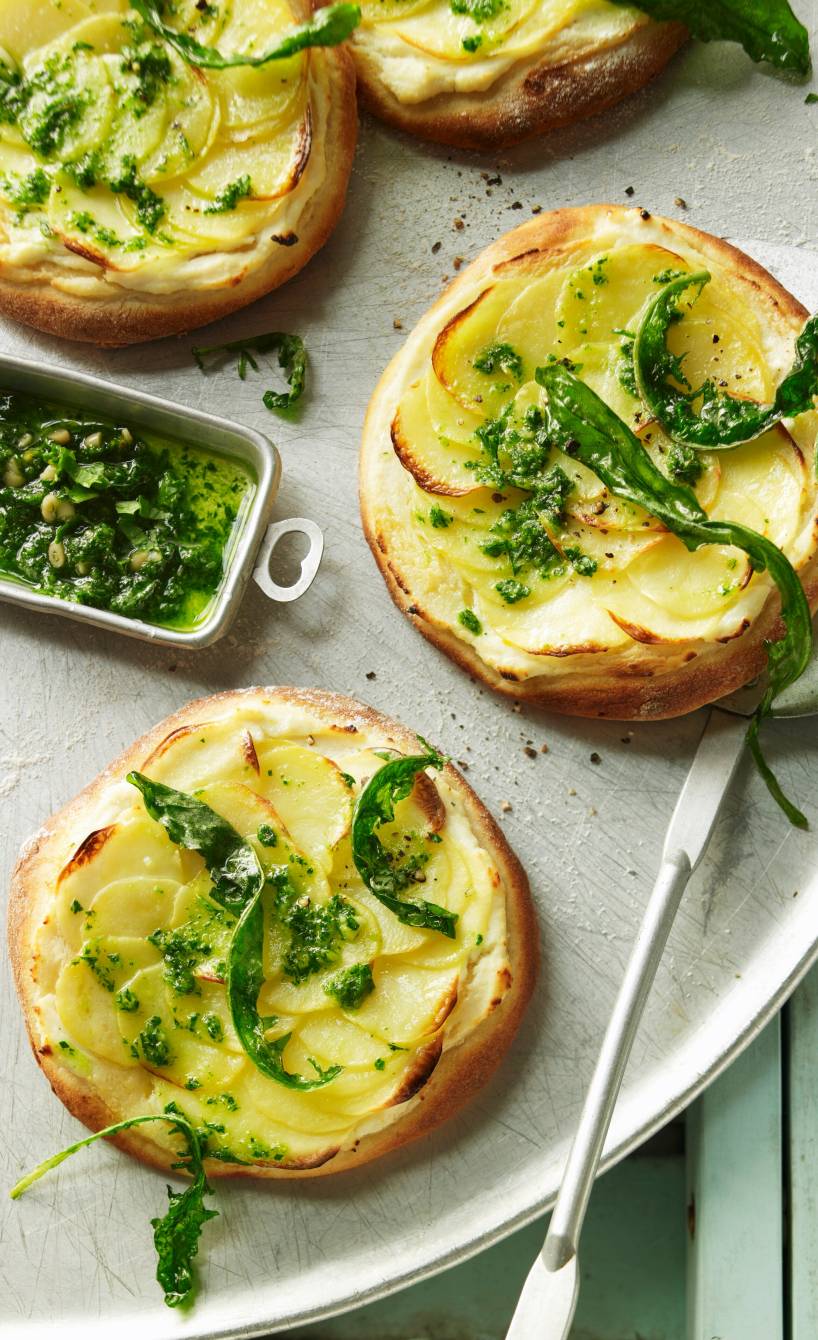 Mehrere Mini-Kartoffelpizza mit Tofu-Soja-Creme und grünem Pesto angerichtet auf einer Servierplatte