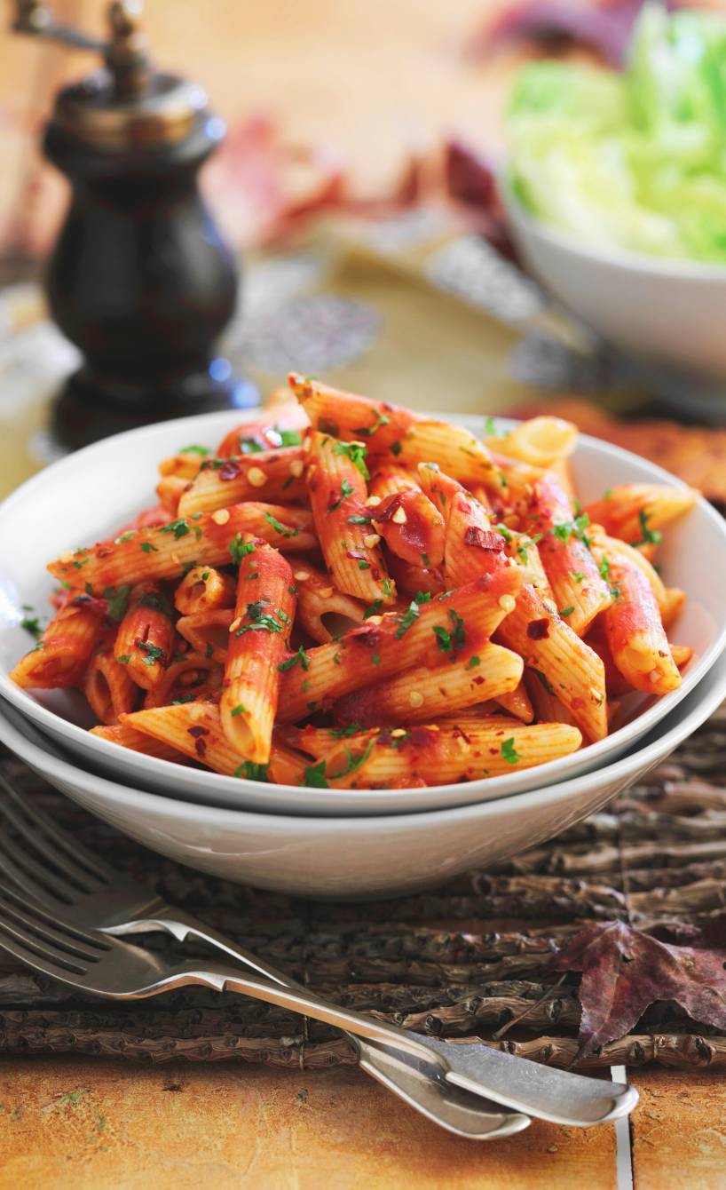 Penne all’arrabbiata in einem tiefen Teller auf einem Tisch, daneben eine Pfeffermühle