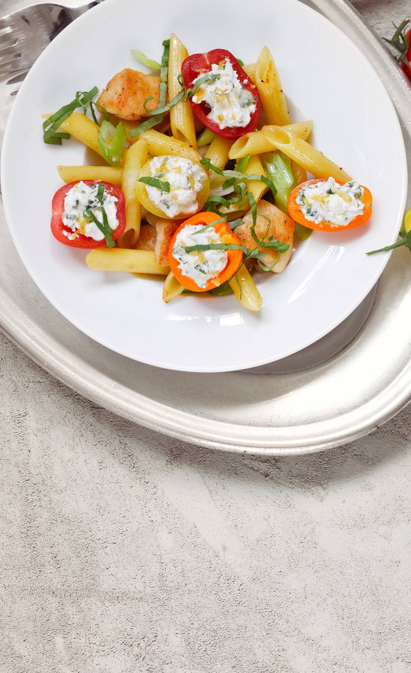 Penne mit gebratener Hähnchenbrust und gefüllten Tomaten mit Frischkäse angerichtet auf einem Pastateller