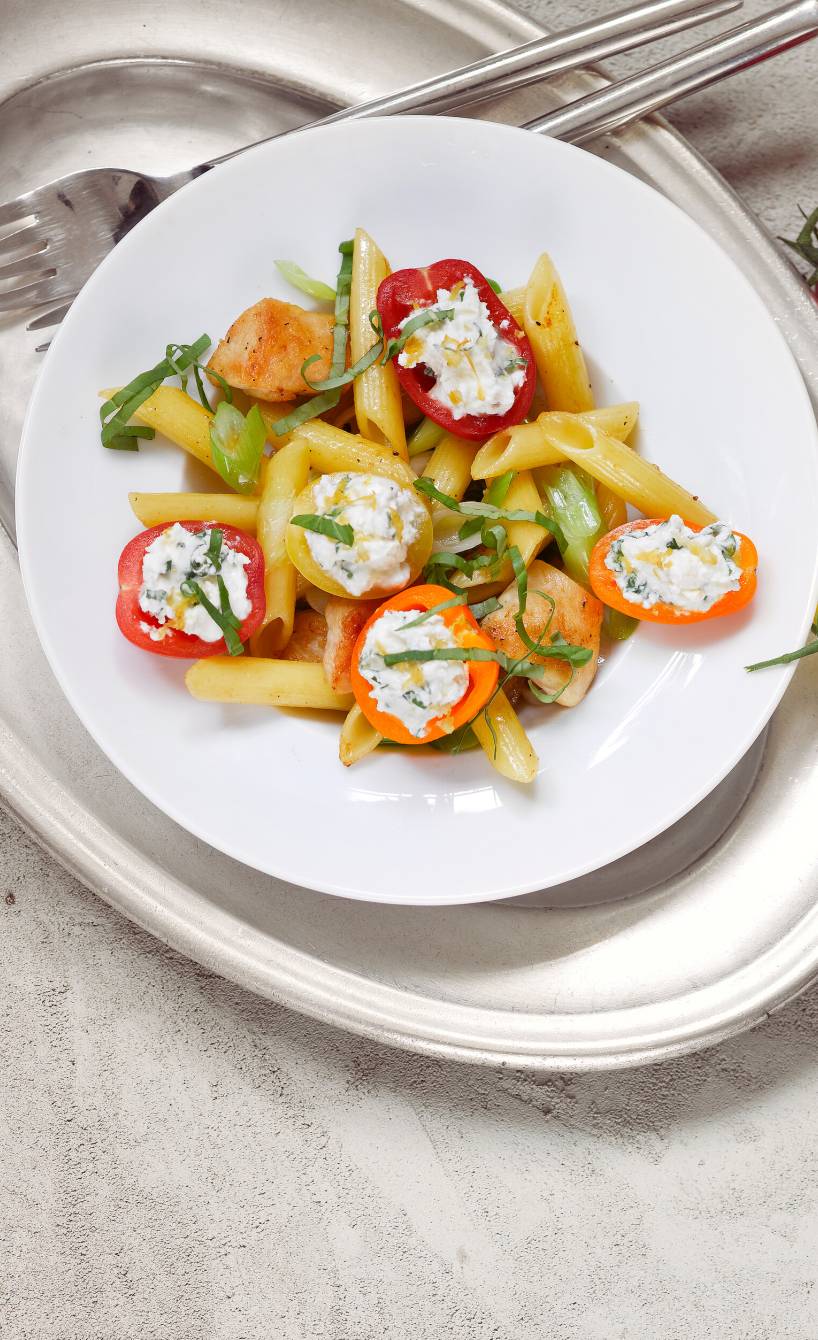 Penne mit gebratener Hähnchenbrust und gefüllten Tomaten mit Frischkäse angerichtet auf einem Pastateller