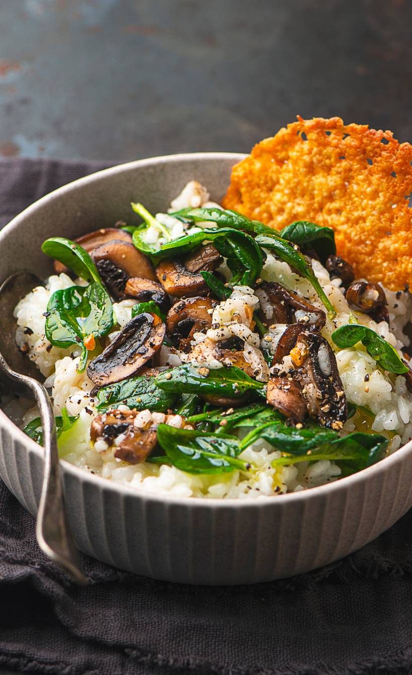 Pilzrisotto in einer Schale mit Spinat und einem runden Parmesanchip