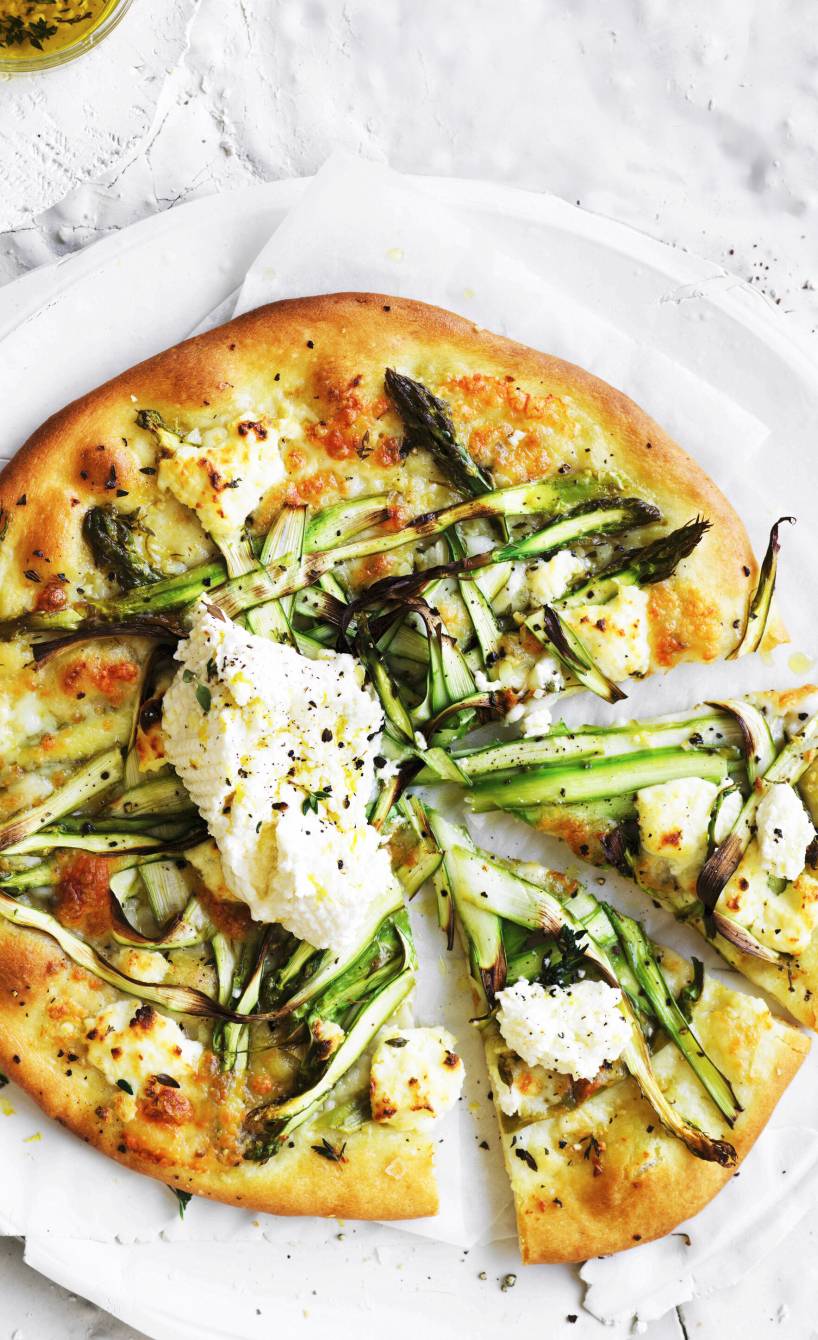 Vegetarische runde Spargelpizza angeschnitten auf einem Teller getoppt mit Ricotta