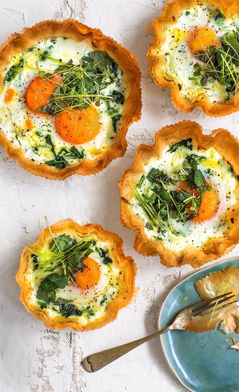 Mehrere selbstgebackene Ricotta-Törtchen aus Filoteig gefüllt mit Ei, Sahne und frischen Kräutern auf einem Tisch