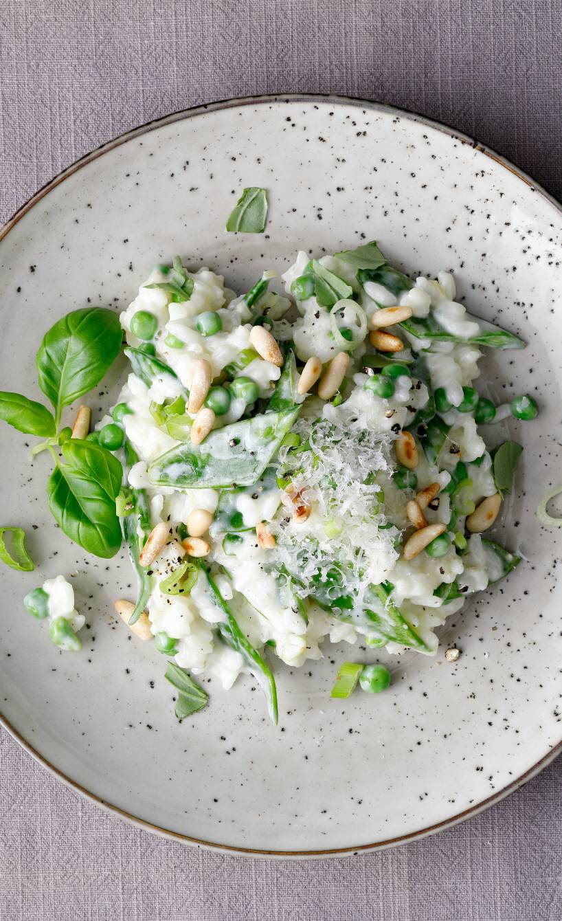 Risotto mit Zuckerschoten, Erbsen und Mascarpone getoppt von Pinienkernen angerichtet auf einem großen Teller