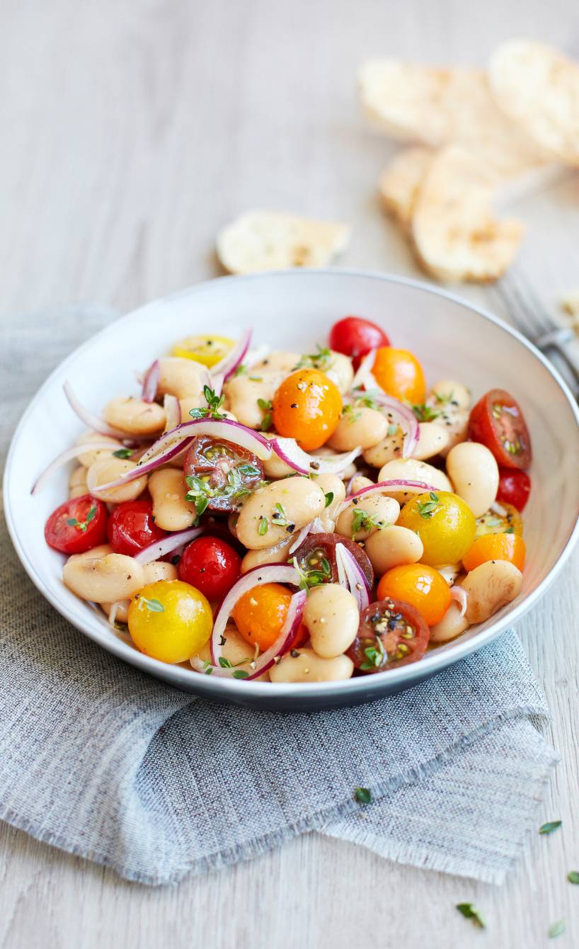 Salat aus weißen Riesenbohnen und Tomaten angerichtet auf einem tiefen Teller