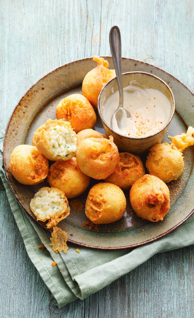 Reisbällchen auf einem Teller, teilweise halbiert mit sichtbarer Füllung, daneben ein Schälchen mit Joghurtdip