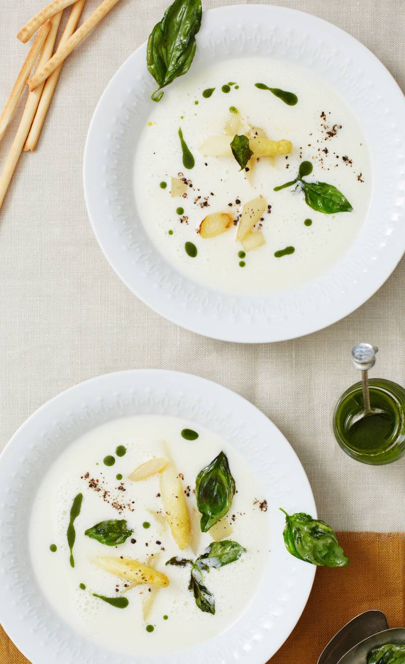 Spargelcremesuppe in zwei Suppentellern getoppt mit gebratenen Spargelstücken und Basilikumöl
