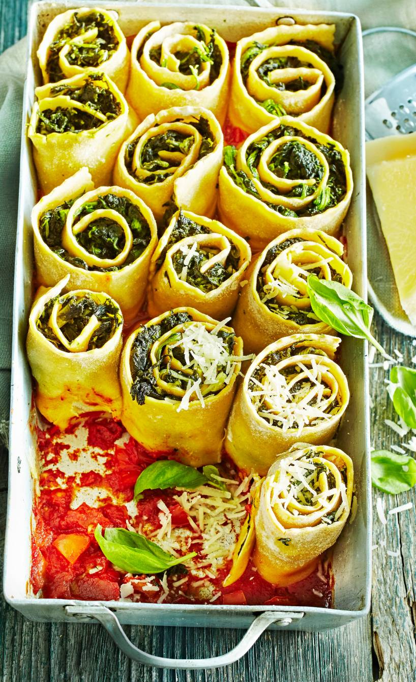 Spinat-Lasagne-Röllchen aufrecht in einer Auflaufform in Tomatensoße mit Parmesan bestreut