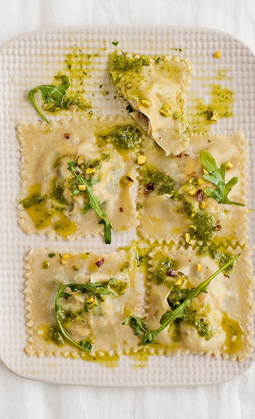 Selbst gemachte Tortelli gefüllt mit Lachs, Ricotta, Rucola und Pistazien auf einem Holzbrett, daneben Pesto