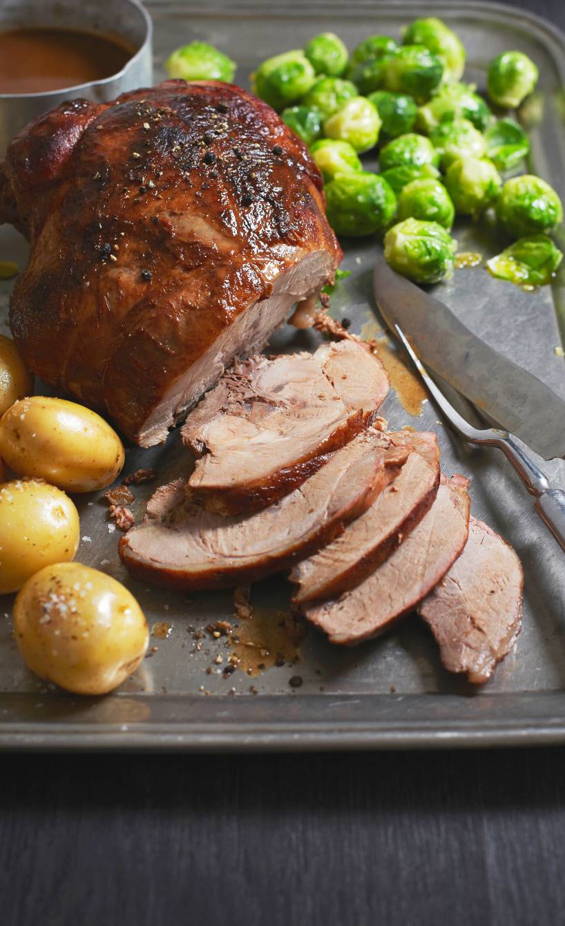 Italienischer Wildschweinbraten angeschnitten auf einer Servierplatte, daneben Kartoffeln, Rosenkohl und Soße
