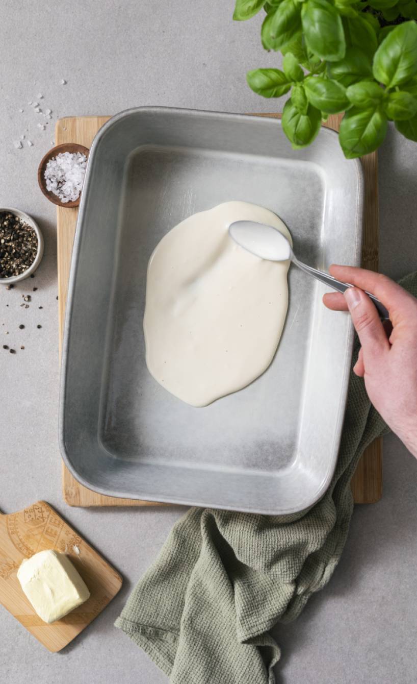 Béchamelsoße wird in einer Auflaufform verteilt