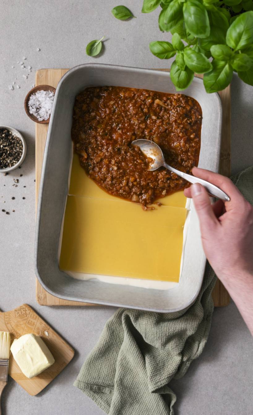 Bolognesesoße wird auf einer Schicht Lasagneplatten in eine Auflaufform geschichtet