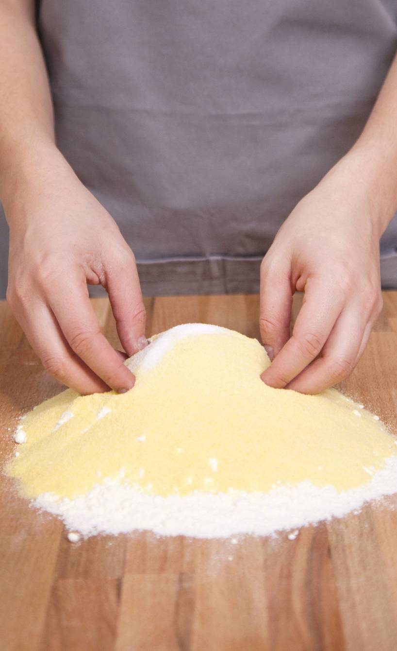 Maccheroni selber machen, Schritt 1: Mehl, Hartweizengrieß und Salz auf die Arbeitsfläche geben und vermen- gen. Die Mischung aufhäufeln und eine Mulde in die Mitte drücken