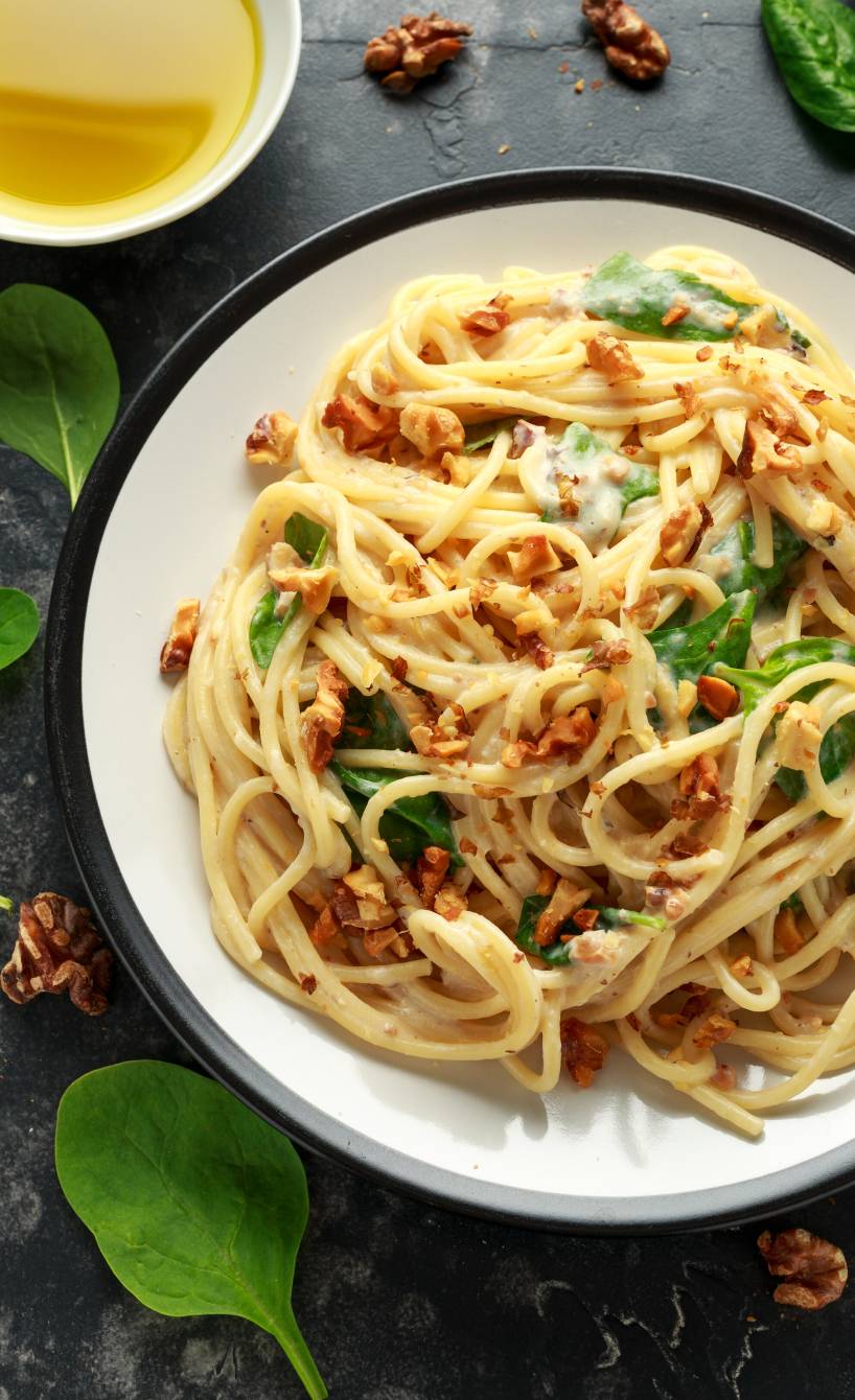Spaghetti in Sahnesoße mit Gorgonzola und Spinat getoppt von Nüssen auf einem Pastateller