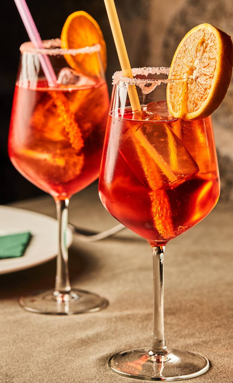 Zwei Gläser mit Aperol Spritz dekoriert mit Orangenscheiben auf einem gedeckten Tisch