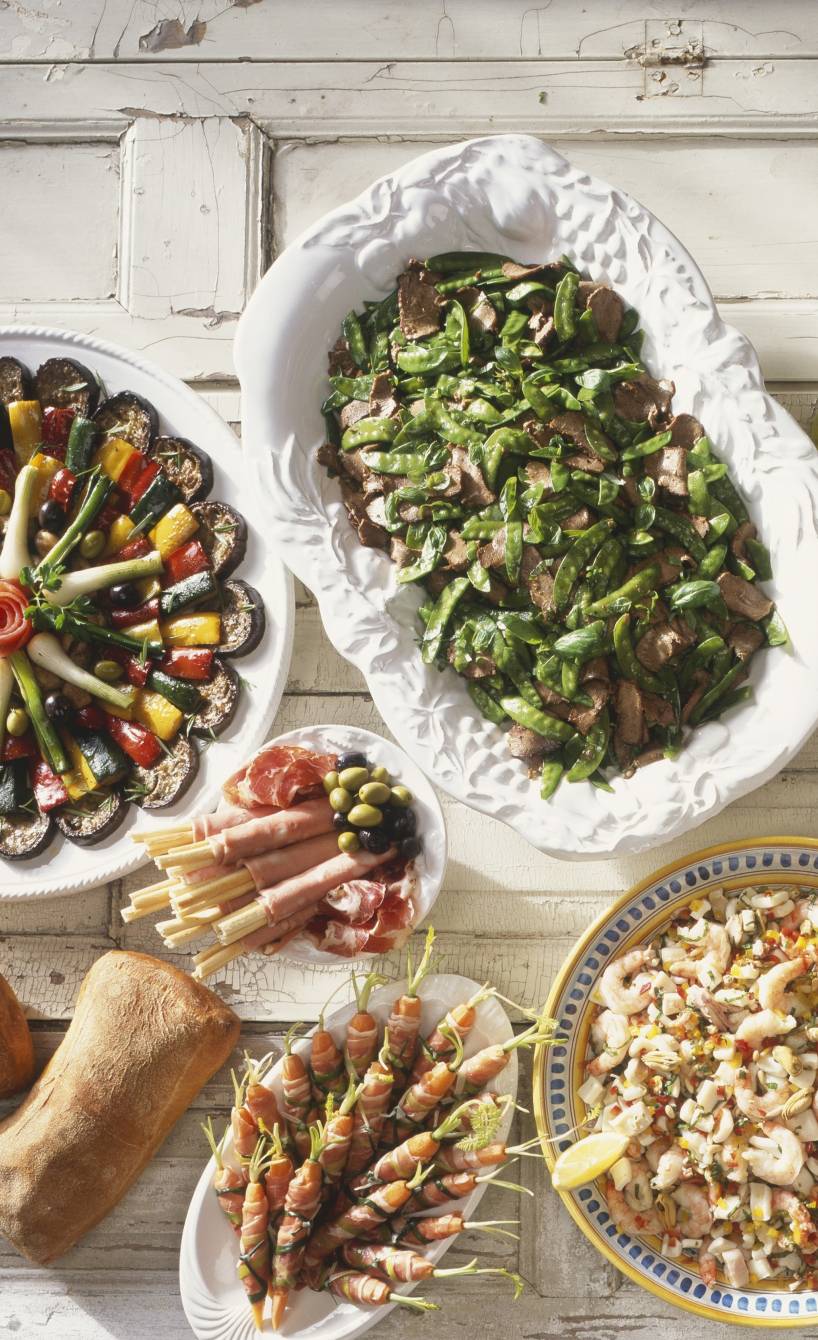 Italienisches Buffet aus Antipasti, Hauptgerichten und Desserts auf einem weißen Holztisch