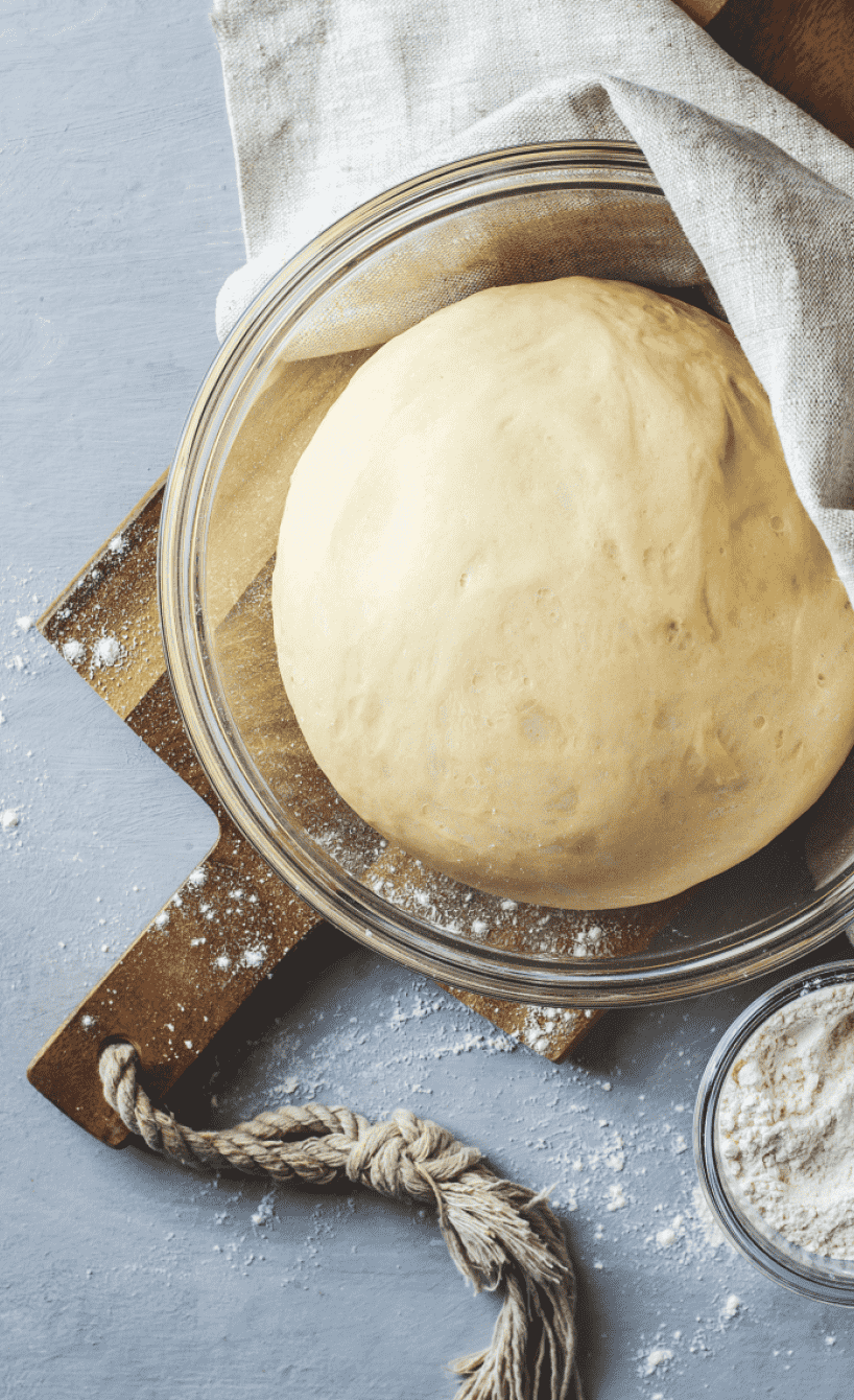 Flammkuchenteig auf einem Tisch, daneben Mehl