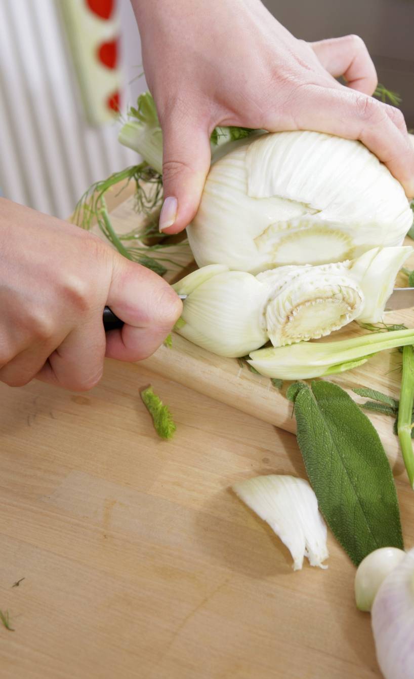 Eine Frau schneidet eine Fenchelknolle auf einem Holzbrett