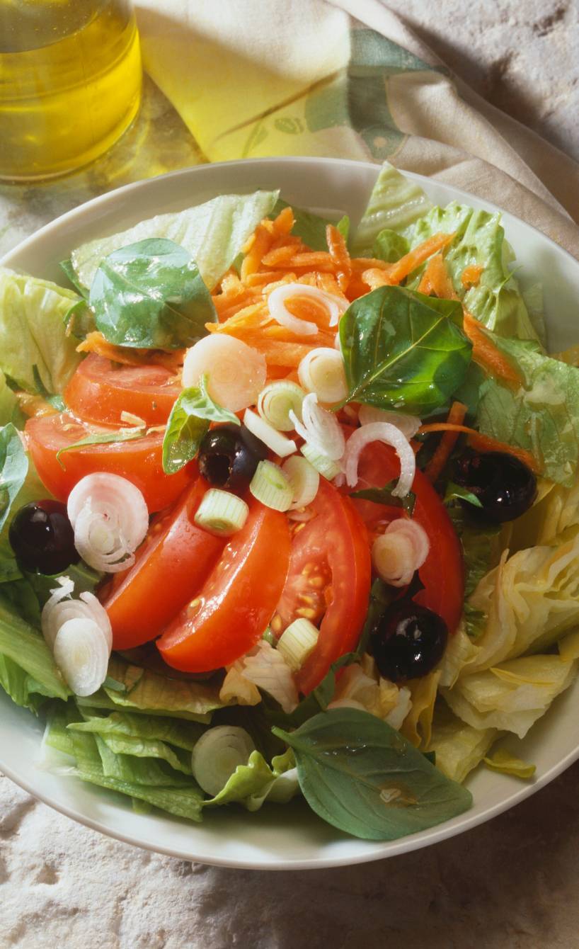 Gemischter italienischer Salat in einem tiefen Teller, daneben Olivenöl in einer Karaffe