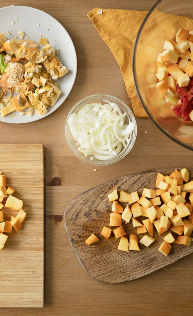 Kürbis nach italienischen Küchentipps in Würfel geschnitten auf einem Holztisch, daneben mehrere Herbstzutaten