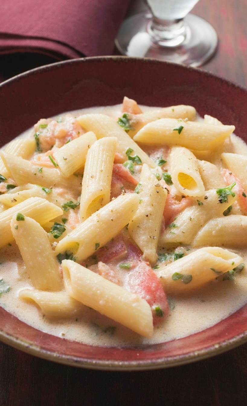 Pasta mit Lachs und Sahnesoße auf einem tiefen Teller, daneben ein Glas Rotwein