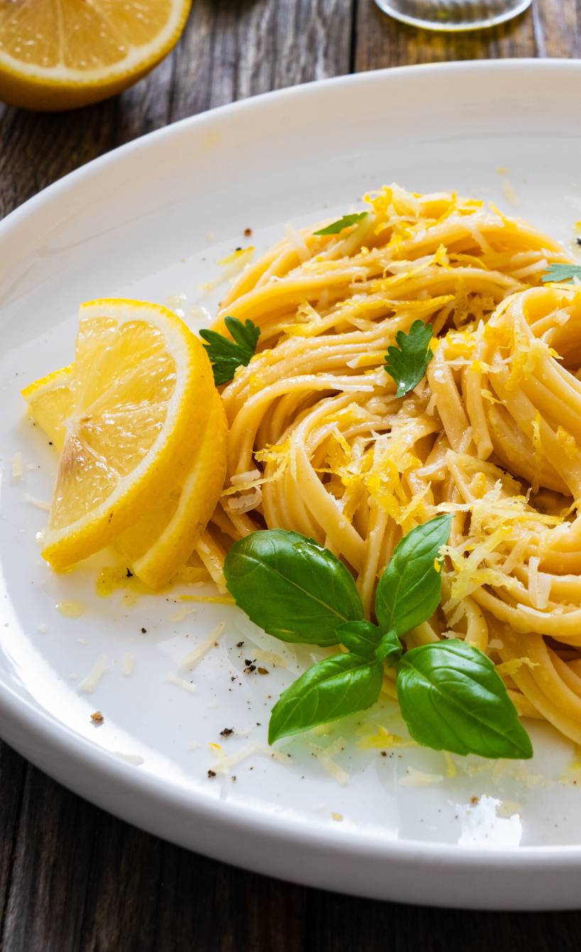 Pasta al limone Spaghetti auf einem Teller angerichtet, daneben Zitronenviertel und Olivenöl